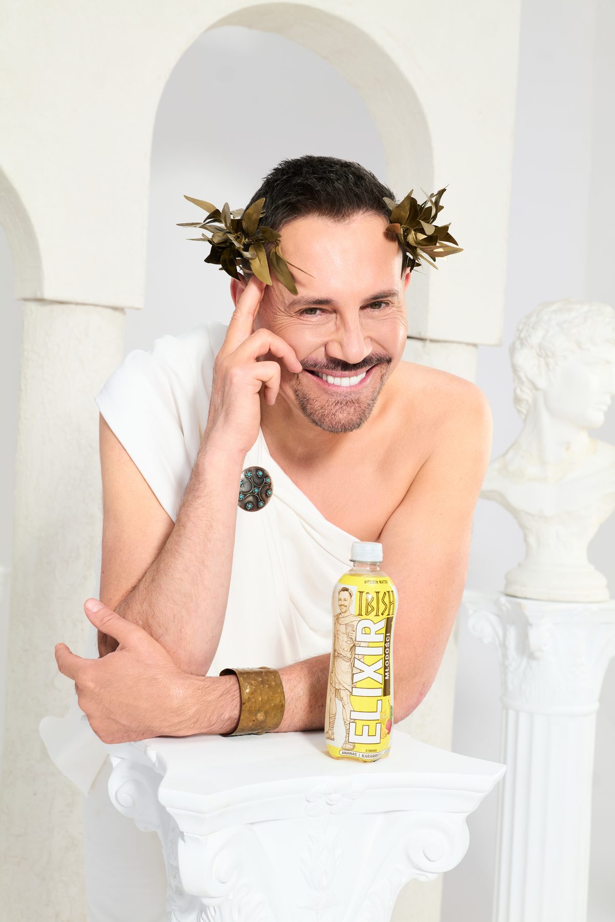 Krzysztof Ibisz w stylizacji antycznej z butelką Elixiru Młodości